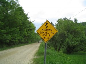 Road sign reading 'winding dirt road, next 9 miles'